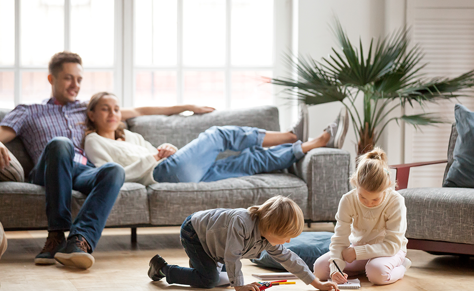 Couple sitting on the couch watching their kids play on the floor