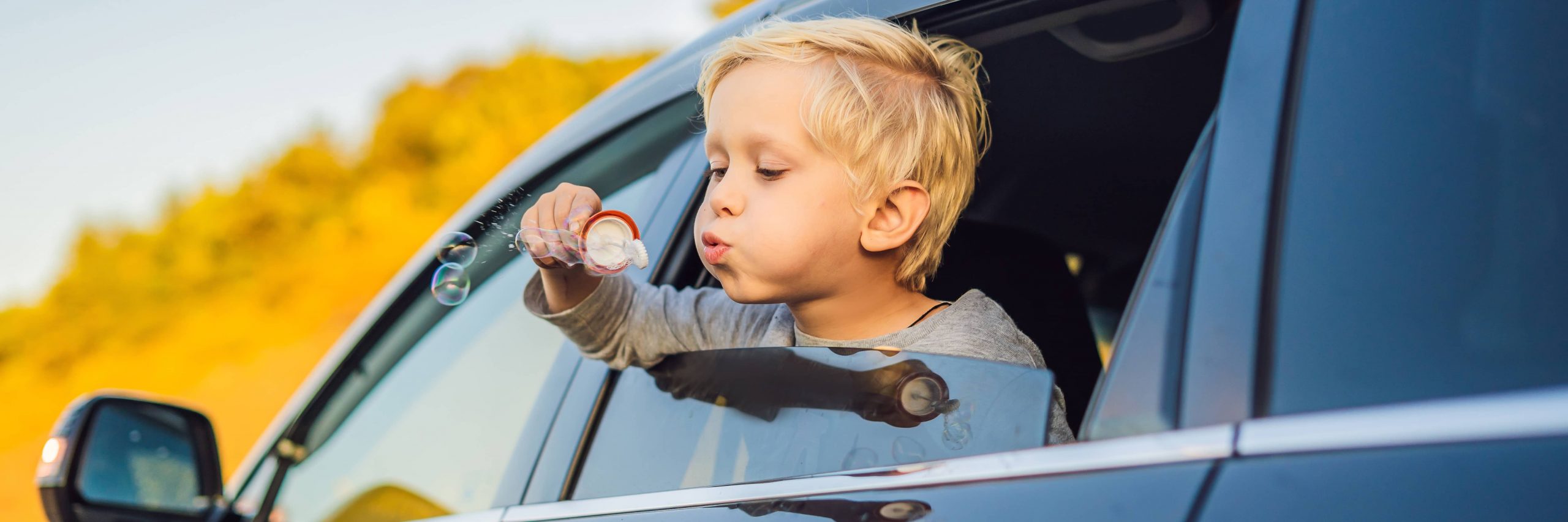 Young child blowing bubbles out of a car window. Benchmark FCU auto loans Chester County webpage.