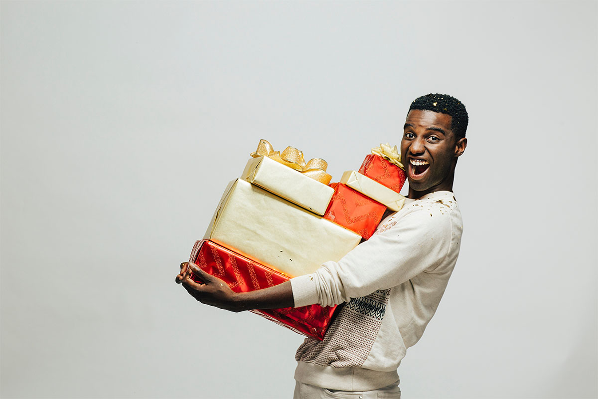 African American man smiling while holding Christmas gifts.