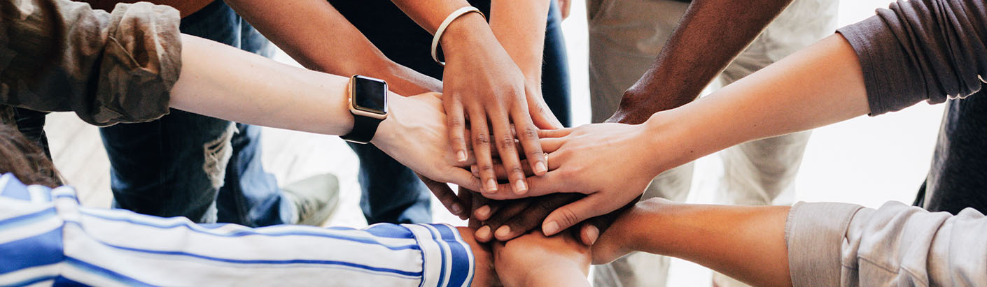 Group of diverse co-workers with their hands in the middle of a huddle.