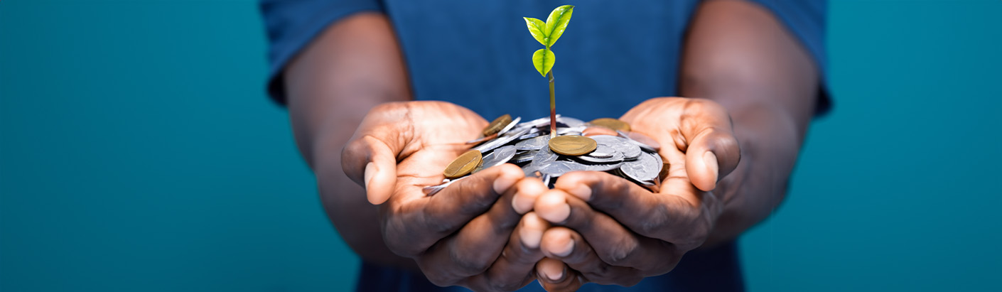 Two hands holding a pile of coins with a small green plant growing out of it.