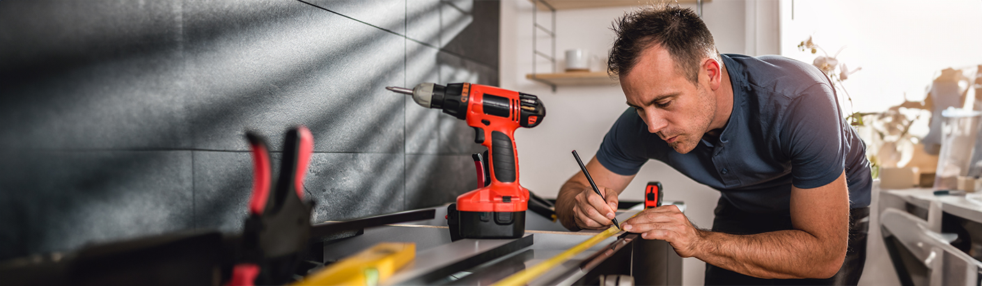 Close up image of a man using measuring tape while working on a countertop.