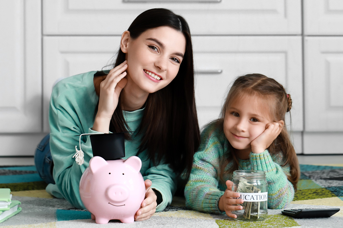 Young mother teaching her daughter about savings with a piggy bank and savings jar.