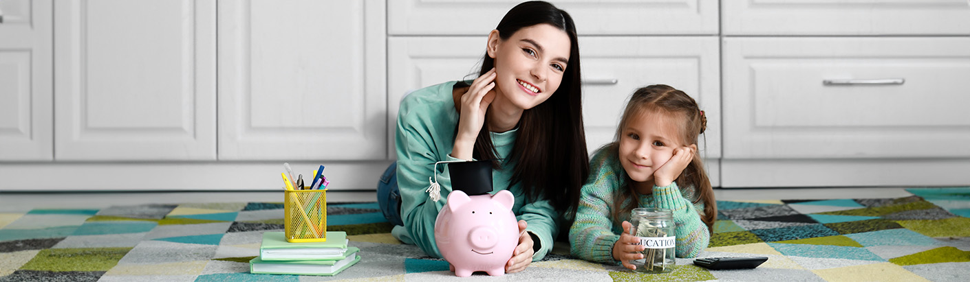 Young mother teaching her daughter about savings with a piggy bank and savings jar.