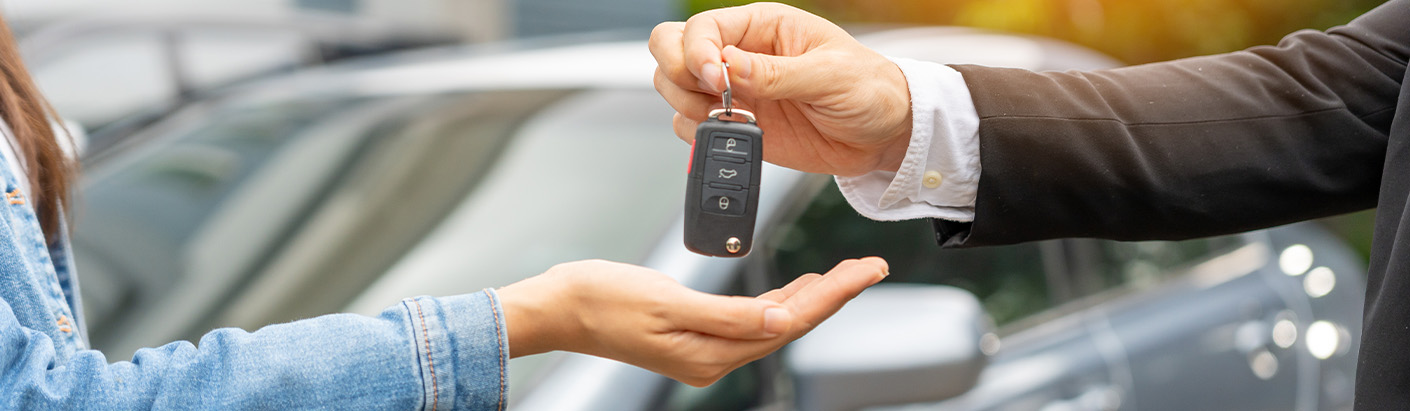 Close up of a car salesman handing car keys to a new buyer.